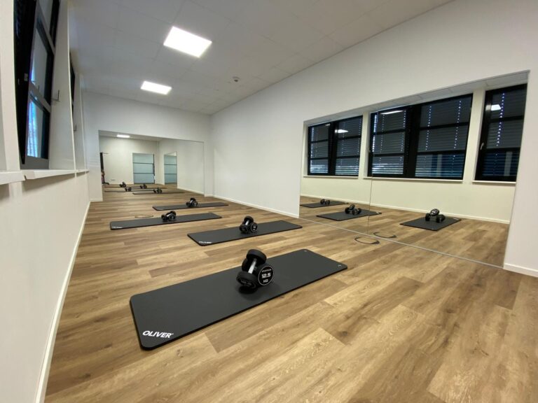 Kursraum im LSZ mit ausgelegten Gymnastikmatten, Kurzhanteln und Spiegelwand